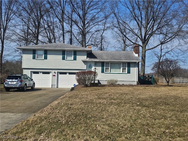 split level home featuring a shingled roof, a chimney, a front lawn, a garage, and aphalt driveway