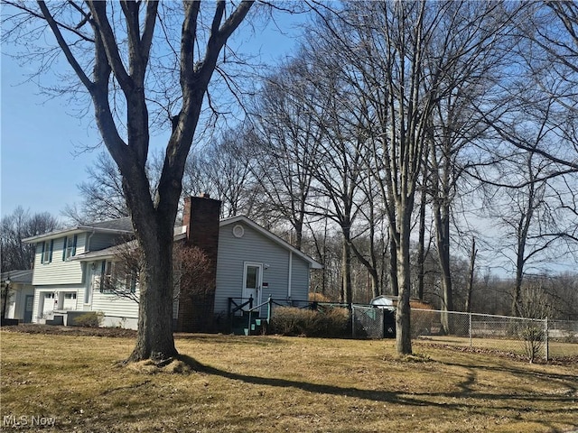 view of property exterior with a lawn, a chimney, a garage, and fence