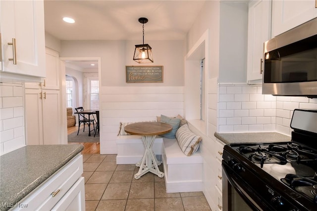 kitchen featuring light tile patterned floors, stainless steel microwave, white cabinets, and range with gas stovetop