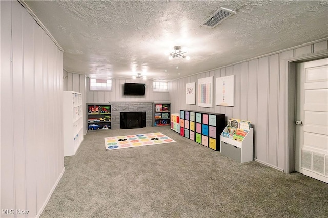 playroom with visible vents, a fireplace, a textured ceiling, and carpet floors