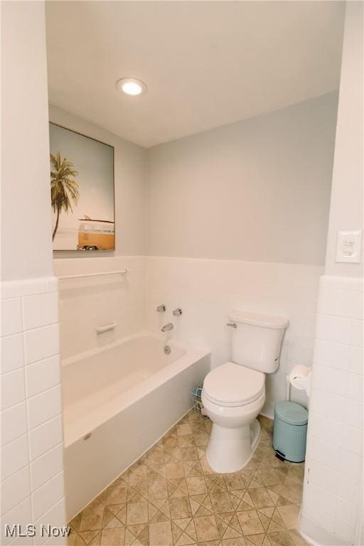 bathroom featuring a garden tub, toilet, and a wainscoted wall