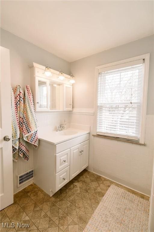 bathroom featuring vanity, visible vents, wainscoting, tile patterned floors, and tile walls