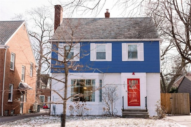 view of front facade with entry steps, fence, and a chimney