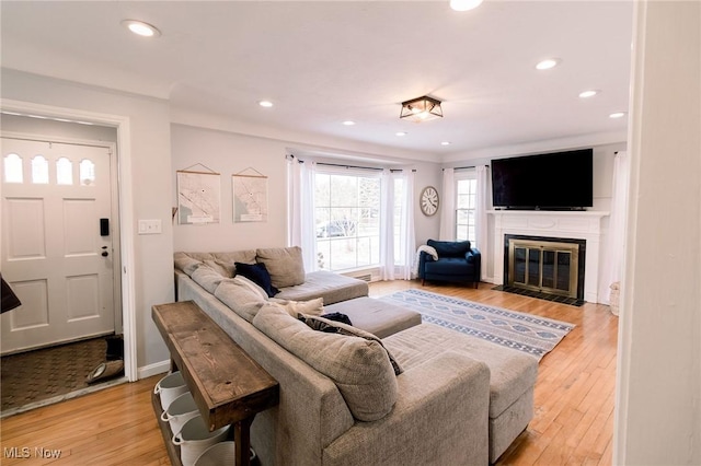 living room featuring a fireplace with flush hearth, recessed lighting, baseboards, and light wood-style floors