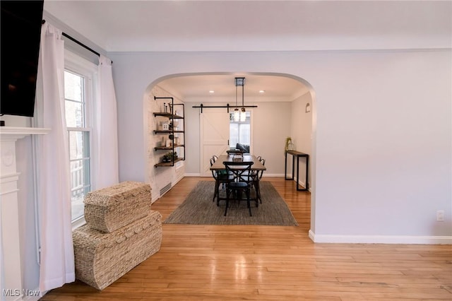 dining space with a barn door, a healthy amount of sunlight, light wood-type flooring, and arched walkways