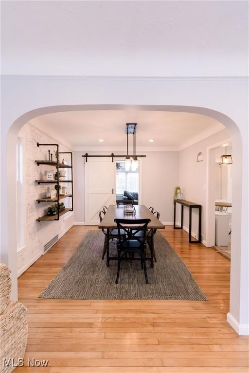 dining space with visible vents, arched walkways, wood finished floors, and a barn door