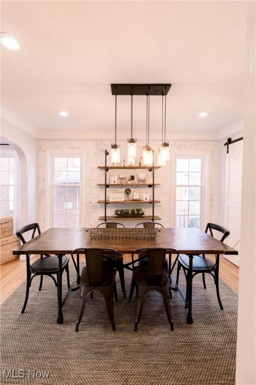 dining area featuring recessed lighting, a barn door, arched walkways, and light wood-style flooring