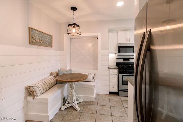 kitchen featuring breakfast area, light tile patterned floors, stainless steel appliances, hanging light fixtures, and white cabinetry