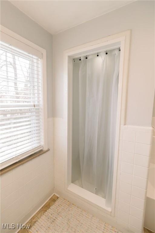 bathroom with tile walls, wainscoting, a shower stall, and a healthy amount of sunlight