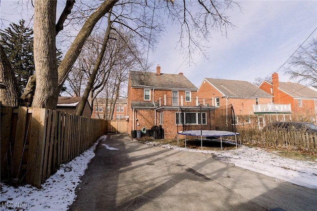 back of house featuring brick siding, a trampoline, a balcony, fence private yard, and a chimney