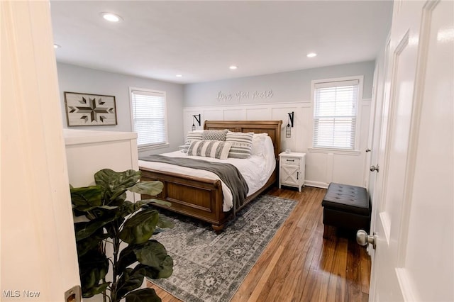 bedroom featuring recessed lighting, a decorative wall, wainscoting, and wood-type flooring