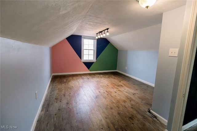 additional living space featuring hardwood / wood-style floors, lofted ceiling, baseboards, and a textured ceiling