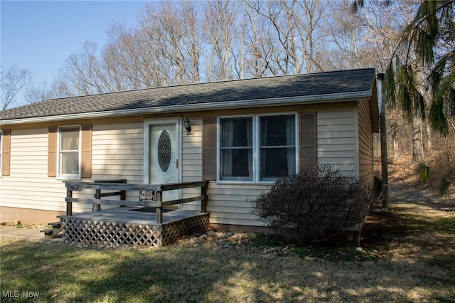 view of front of home featuring a front lawn, a deck, and a shingled roof