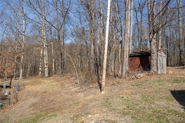 view of yard with an outdoor structure, a storage unit, and a wooded view