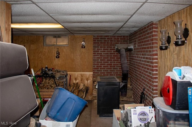 interior space featuring a paneled ceiling, brick wall, wood walls, and a wood stove