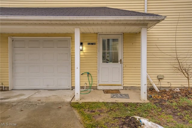 view of exterior entry with a garage, concrete driveway, and roof with shingles