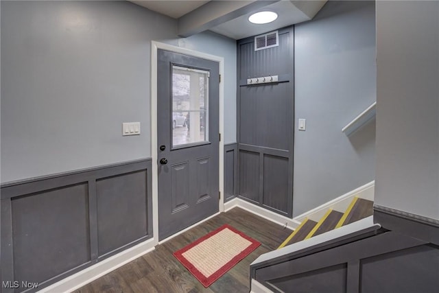 entryway with visible vents, dark wood-type flooring, beamed ceiling, wainscoting, and a decorative wall