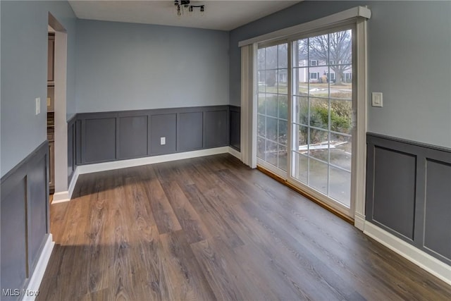 unfurnished dining area featuring a wainscoted wall, a decorative wall, and dark wood-style flooring