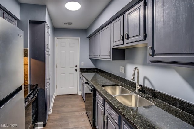 kitchen featuring visible vents, black appliances, a sink, wood finished floors, and dark stone counters