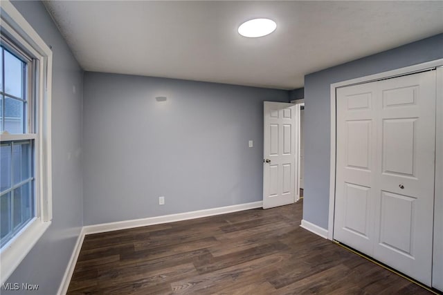 unfurnished bedroom with a closet, dark wood-type flooring, and baseboards