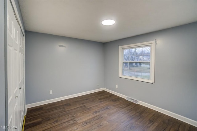 empty room with visible vents, dark wood-style floors, and baseboards