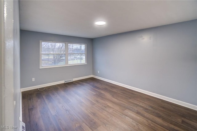 empty room with dark wood finished floors, baseboards, and visible vents