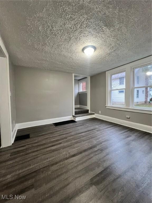 empty room with dark wood-type flooring, baseboards, and a textured ceiling