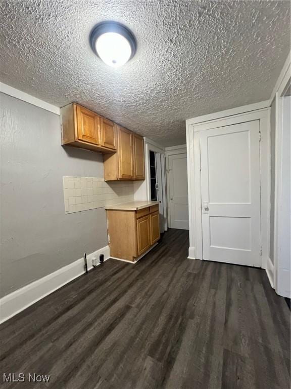 kitchen with brown cabinetry, baseboards, dark wood-type flooring, light countertops, and a textured ceiling