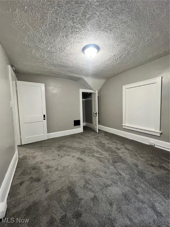 unfurnished bedroom featuring lofted ceiling, a textured ceiling, a closet, carpet flooring, and baseboards