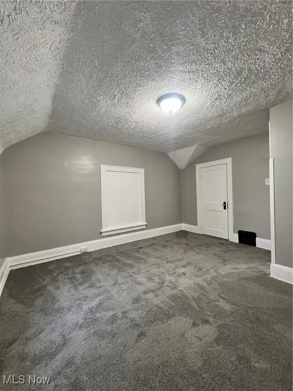 bonus room featuring lofted ceiling, baseboards, dark carpet, and a textured ceiling