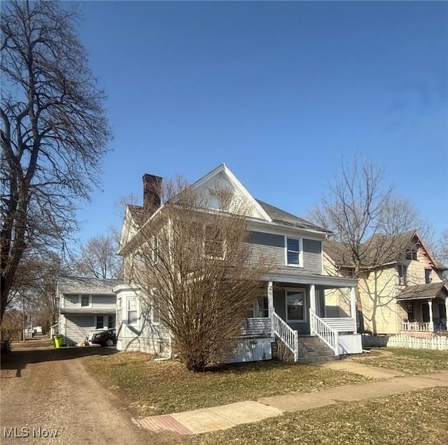 view of front facade with driveway, covered porch, and a chimney