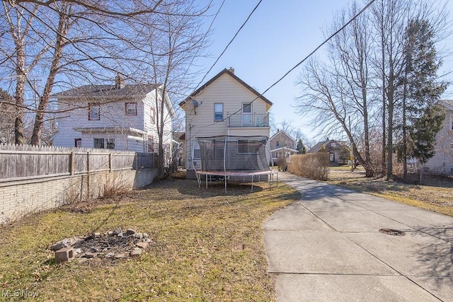 back of property with a trampoline, fence, and a lawn