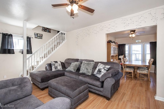 living room with ceiling fan, stairway, and light wood-style flooring