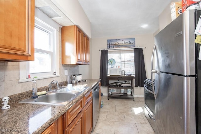 kitchen featuring brown cabinets, a sink, backsplash, stainless steel appliances, and light tile patterned flooring