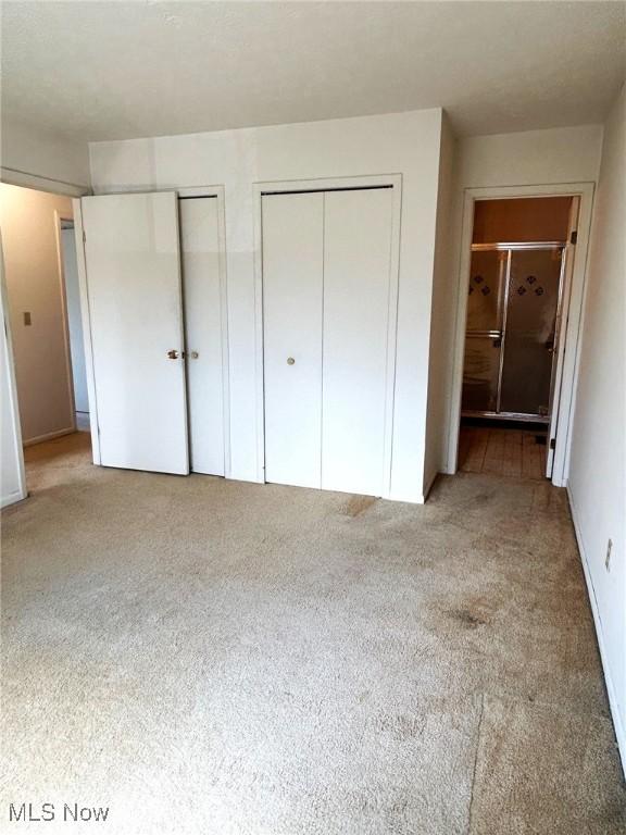 unfurnished bedroom with light carpet, two closets, and ensuite bath