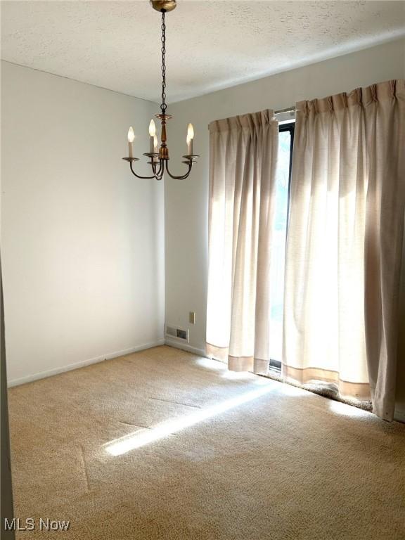 carpeted empty room with a notable chandelier, baseboards, visible vents, and a textured ceiling