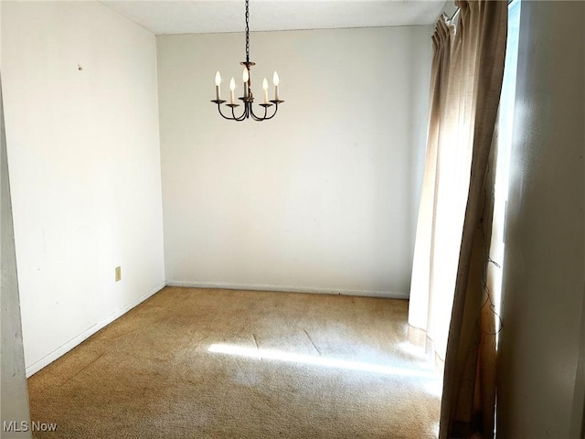 carpeted spare room with baseboards and a chandelier