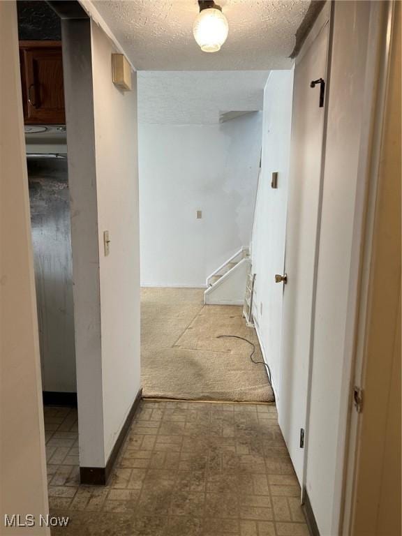 corridor with tile patterned floors, carpet flooring, and a textured ceiling