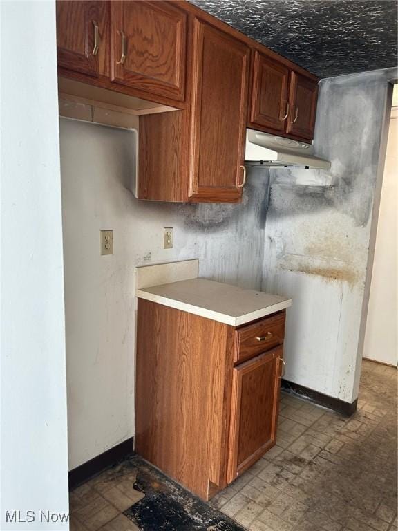 kitchen with light countertops, baseboards, under cabinet range hood, and brown cabinets