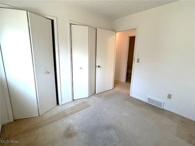 unfurnished bedroom featuring carpet, visible vents, and two closets