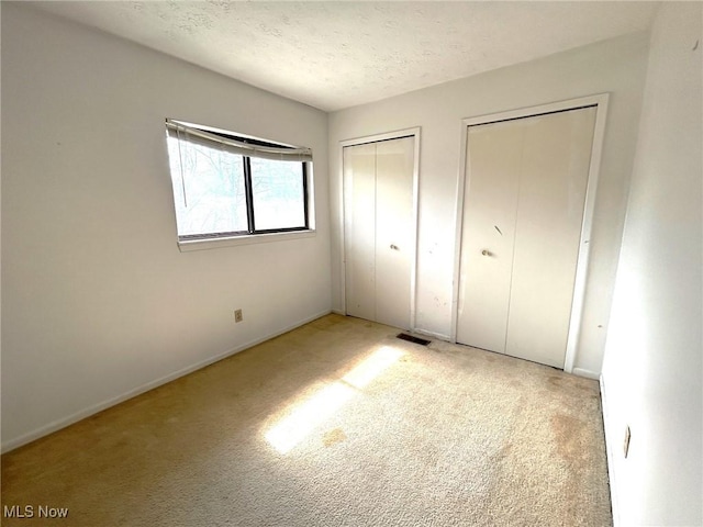 unfurnished bedroom with visible vents, multiple closets, a textured ceiling, and carpet floors