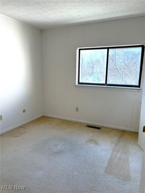 carpeted empty room with baseboards, visible vents, and a textured ceiling