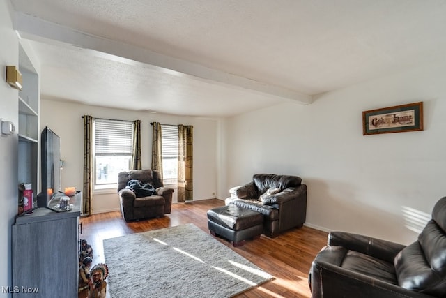 living area with beam ceiling, wood finished floors, baseboards, and a textured ceiling