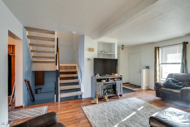 living area featuring stairs, beam ceiling, wood finished floors, and a textured ceiling