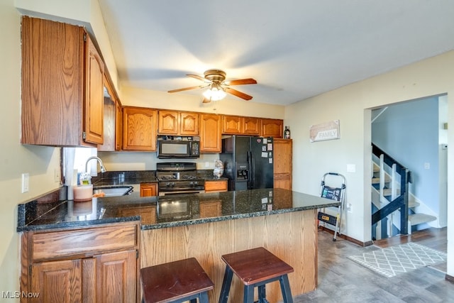 kitchen with ceiling fan, dark stone counters, a peninsula, black appliances, and a sink