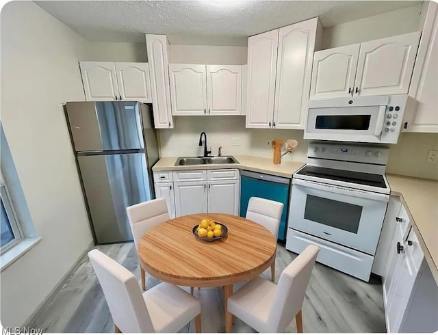 kitchen featuring white appliances, white cabinets, light countertops, and a sink