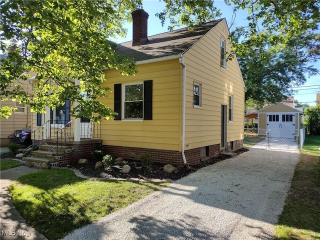 view of front of home featuring gravel driveway, roof with shingles, a chimney, a garage, and a gate