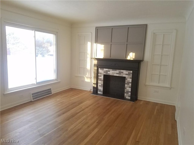 unfurnished living room featuring visible vents, a fireplace, baseboards, and wood finished floors