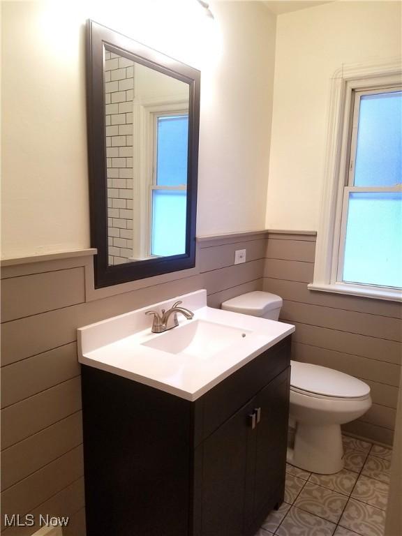 bathroom with a wainscoted wall, toilet, vanity, and tile patterned flooring