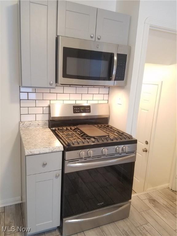 kitchen with wood tiled floor, light stone counters, tasteful backsplash, and stainless steel appliances